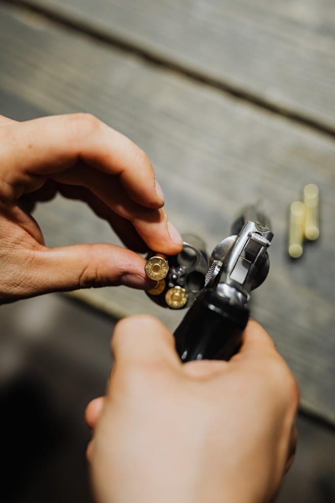 Hands of a Person Holding Silver and Black Gun With Bullets